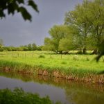 Picture of a canal in bright sunshine but dark clouds in the background