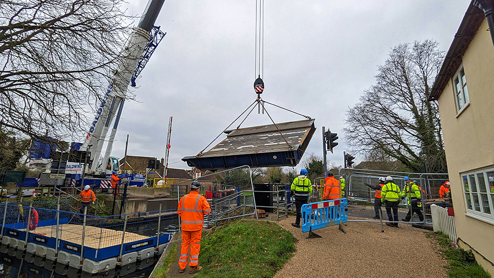 Picture of a bridge hanging from a crane while being lifted over a canal