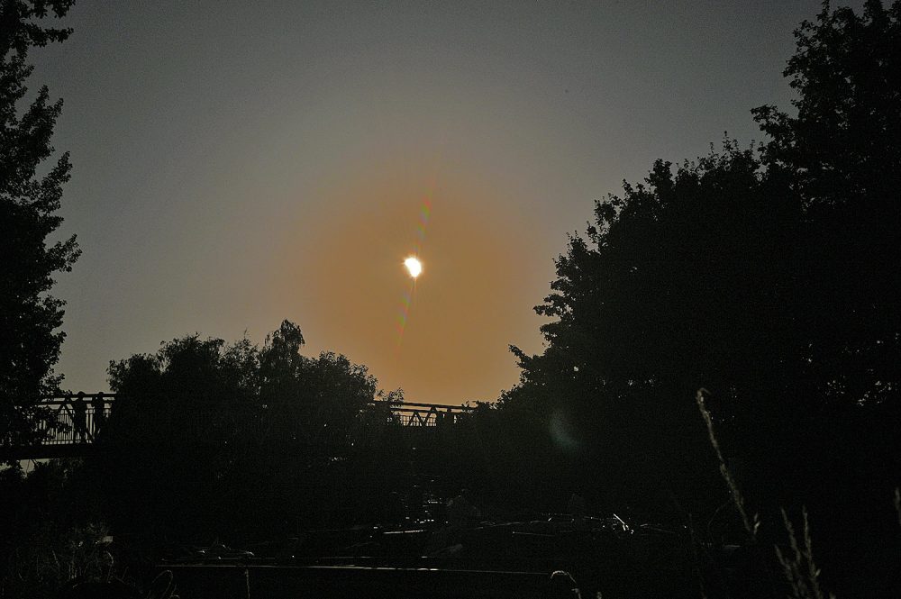 Picture of a partial solar eclipse above a canal with a footbridge